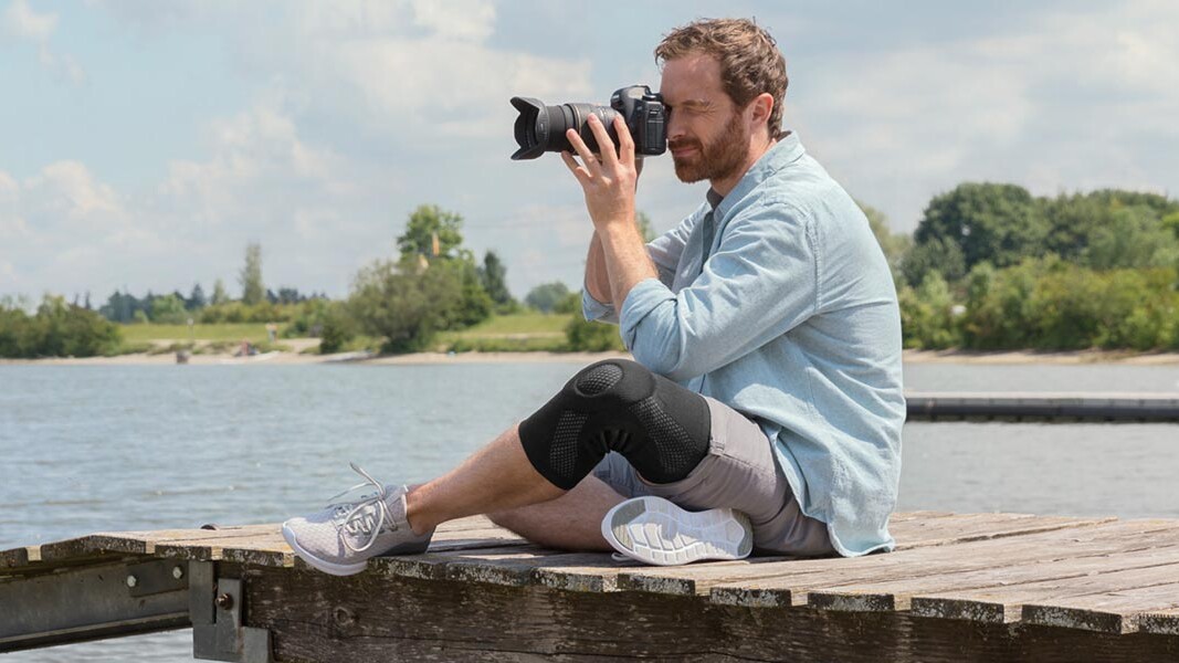 Ein Fotograf sitzt auf einem Steg. Er trägt eine Juzo Kniebandage Ein Fotograf sitzt auf einem Steg. Er trägt eine Juzo Kniebandage