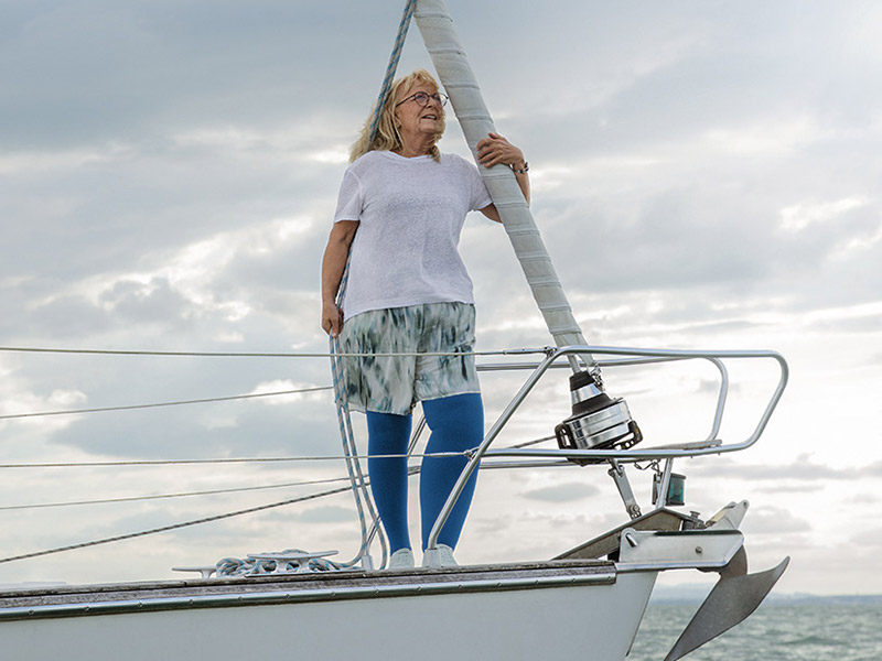 Frau mit einem Lymphödem steht auf dem Deck eines Bootes. Sie trägt blaue Kompressionsstrümpfe Frau mit einem Lymphödem steht auf dem Deck eines Bootes. Sie trägt blaue Kompressionsstrümpfe