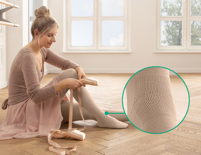 Kvinde i ballerinaoutfit med Juzo Expert med funktionszone vrist sidder på gulvet og tager tåspidssko på