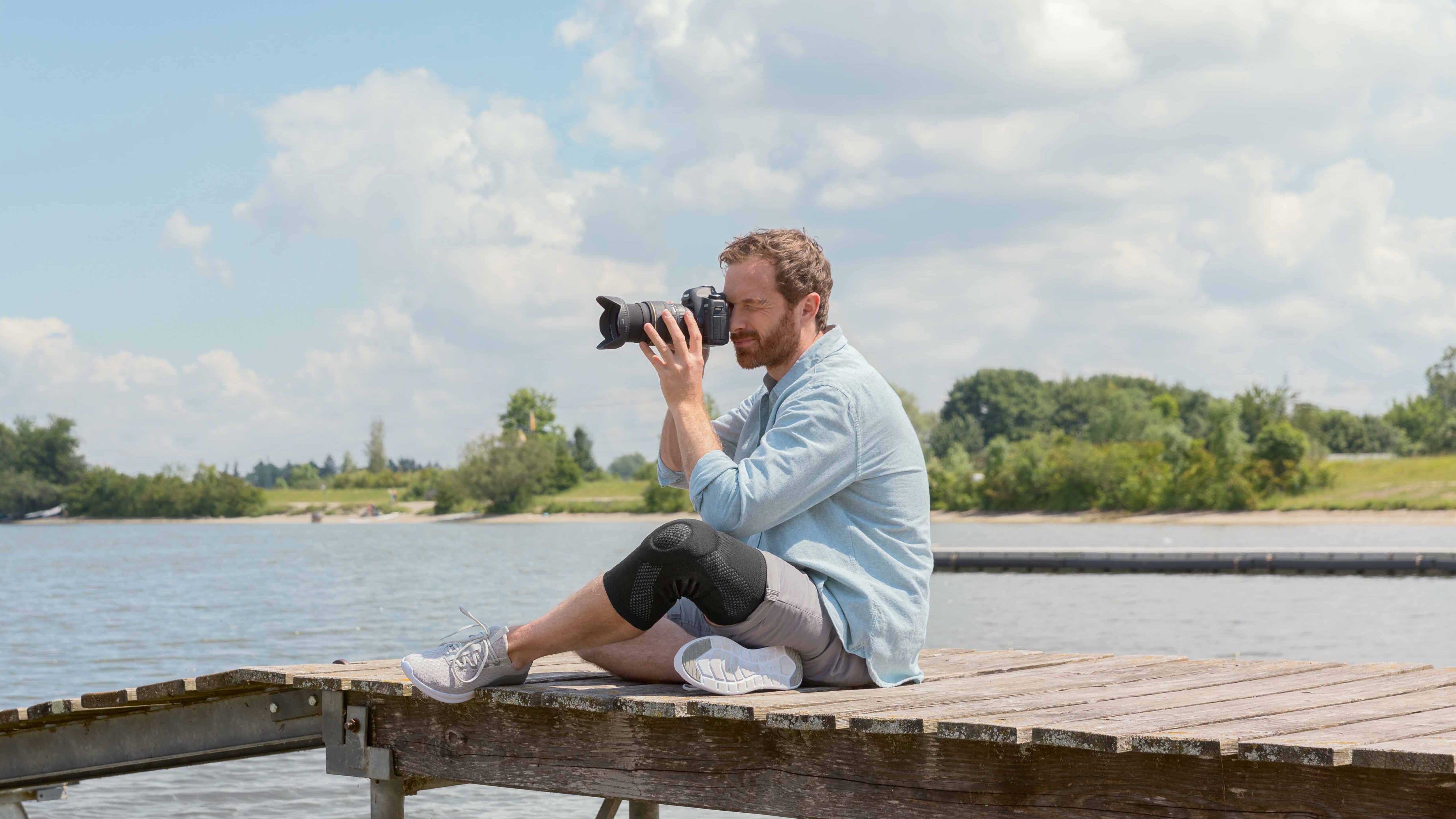 Un photographe est assis sur un ponton. Il porte une genouillère Juzo