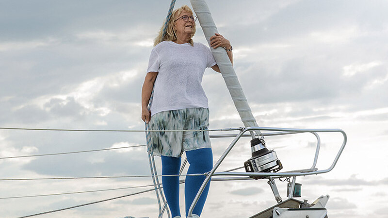 En kvinde med lymfødem står på dækket af en båd. Hun har blå kompressionsstrømper på En kvinde med lymfødem står på dækket af en båd. Hun har blå kompressionsstrømper på
