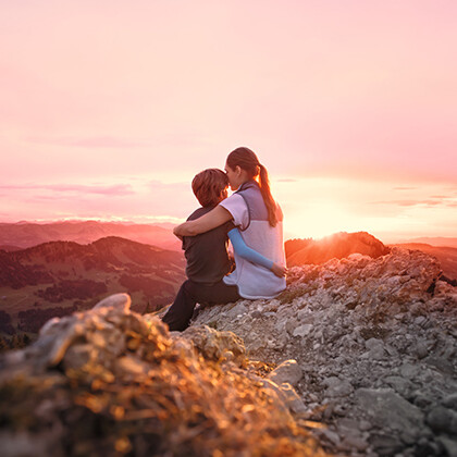 Scar Management A mother sits on a mountain peak with her child in her arms and watches the sunset.
