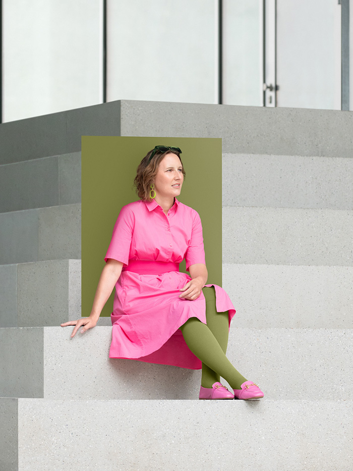 Pure Olive A woman in a pink dress sits on large steps wearing a Pure Olive compression garment