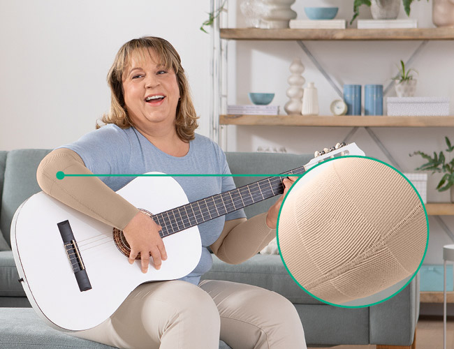 Kvinde med Juzo Expert med funktionszone albue sidder på sofaen og spiller guitar