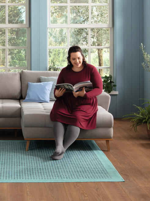 Woman sitting on her couch, smiling and reading a magazine