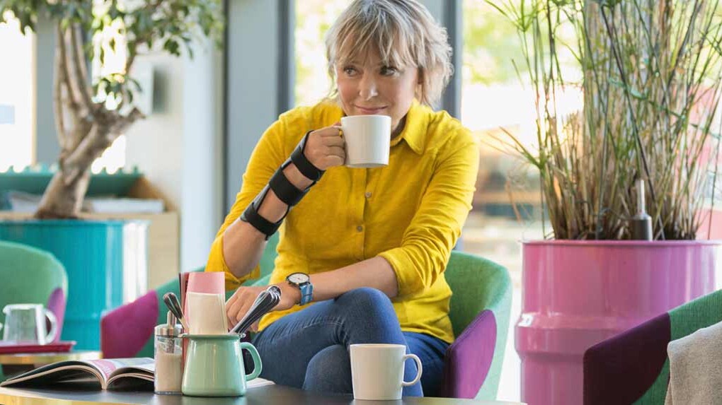 Frau trägt JuzoPro Manu Xtec Handgelenkorthese und hält eine Tasse in der Hand Frau trägt JuzoPro Manu Xtec Handgelenkorthese und hält eine Tasse in der Hand