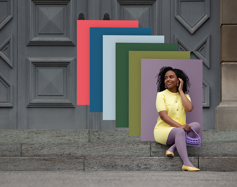 Una donna è seduta su una scala in città. Dietro di lei si vedono cartelle colori rettangolari nei nostri nuovi colori di tendenza