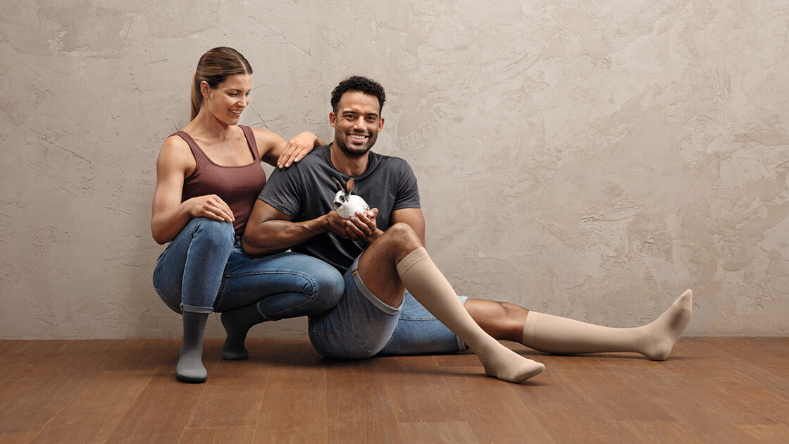 Um casal de desportistas está agachado no chão. Ambos usam meias de compressão Juzo Intenso. O homem tem um coelhinho na mão.