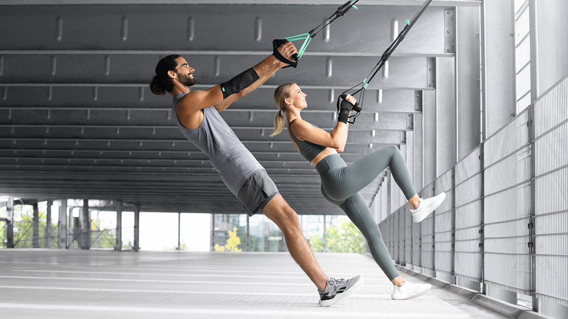 A man and a woman are working out in an underground car park using a TRX strap A man and a woman are working out in an underground car park using a TRX strap