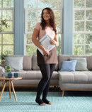 Woman standing in front of her couch, smiling and holding some papers